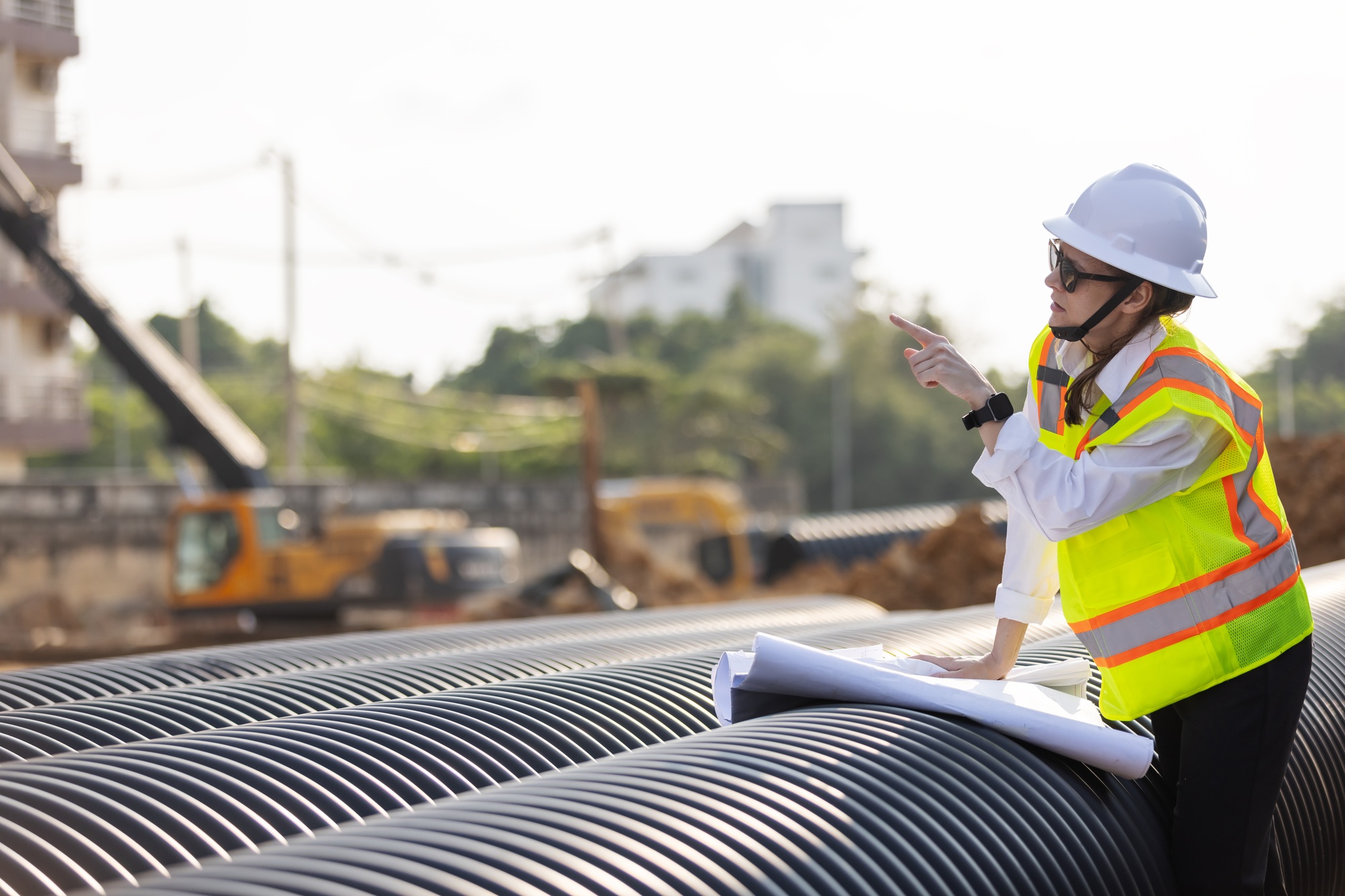 A female engineer examines construction plans on large drainage pipes at a construction site