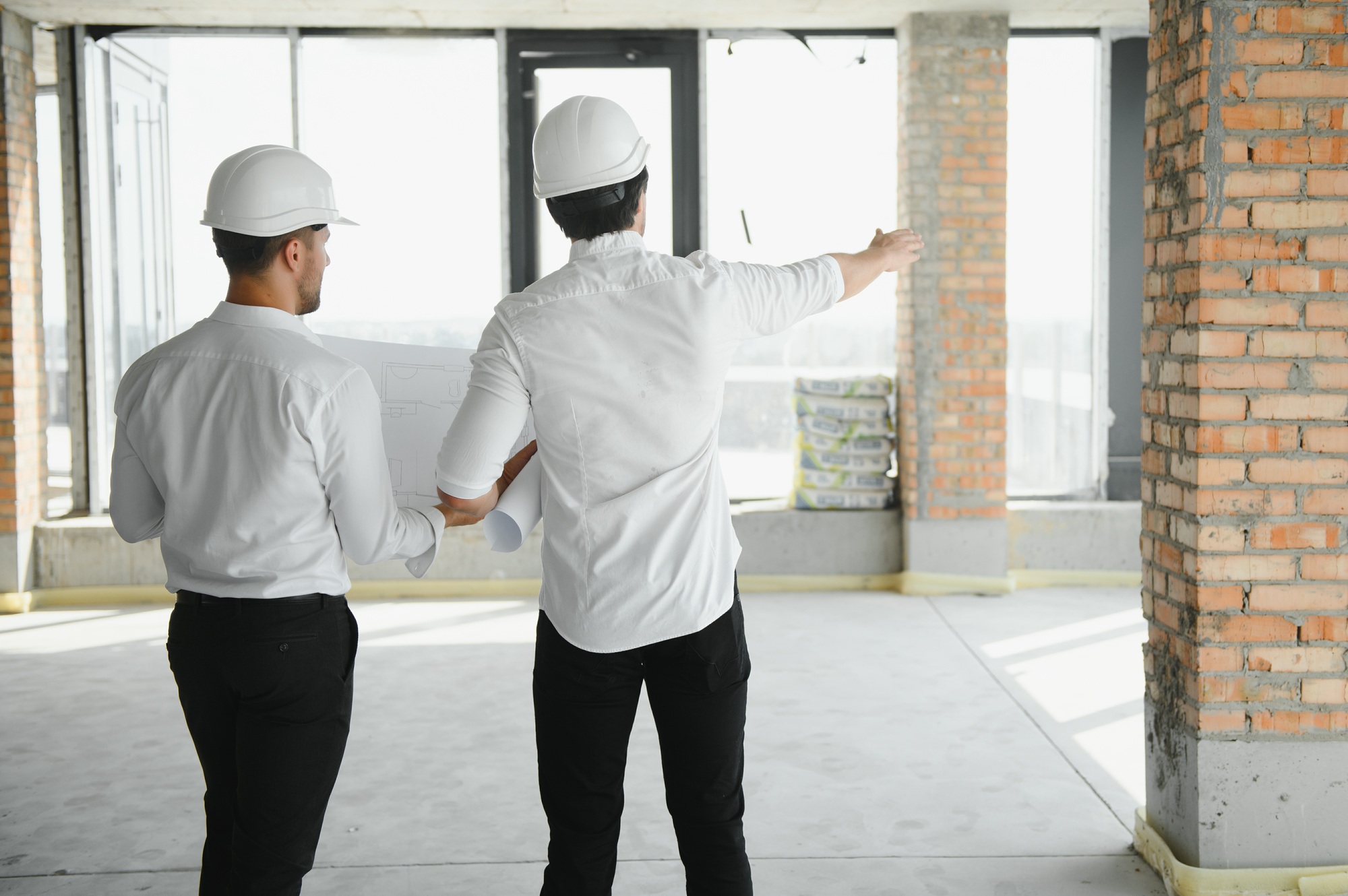 Two civil engineers or architects man inspecting construction of house.